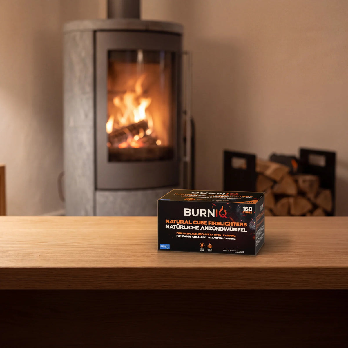 BURNIQ Anzündwürfel-Box auf einer Holzbank vor einem Kaminofen mit Feuer